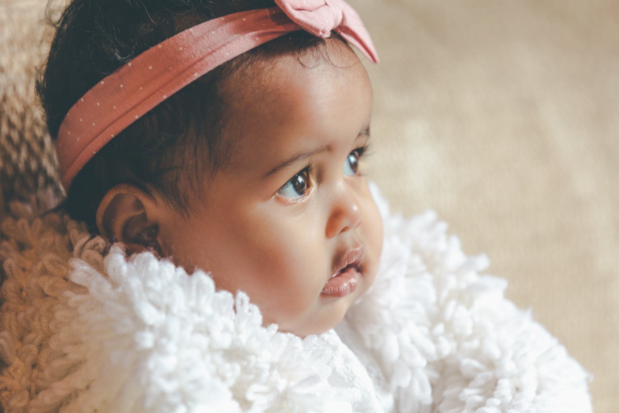 A baby girl with a pink bow headband, looking up