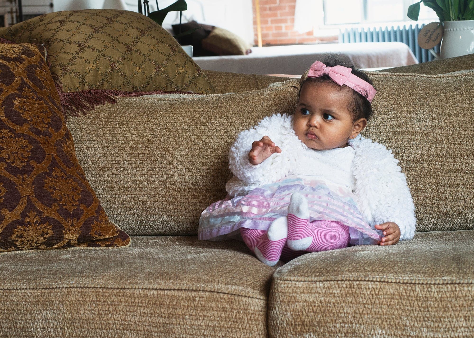 A baby girl in a white cardigan sitting on the sofa