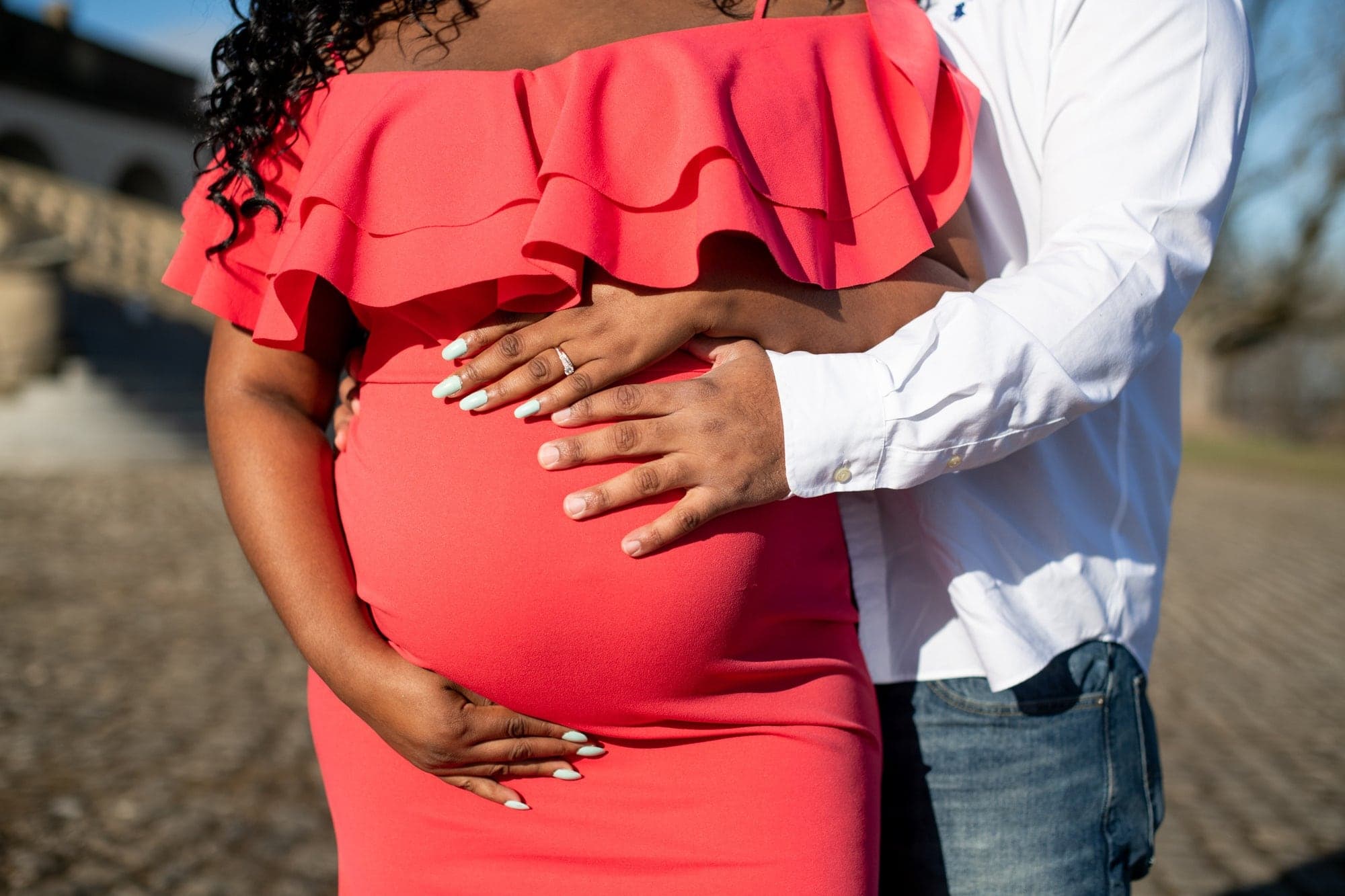 A father's hands and a mother's hands together on her bump in a red dress