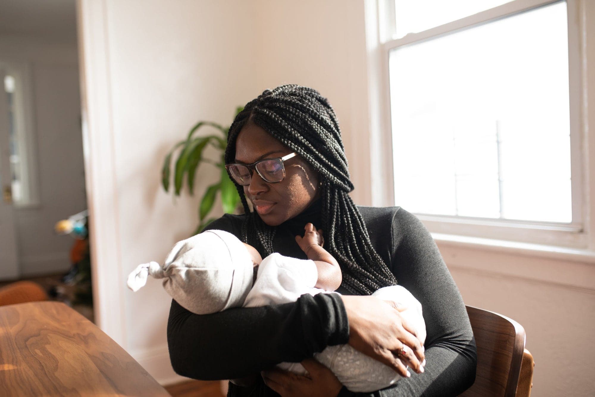 A mother in braids holding her newborn by the window