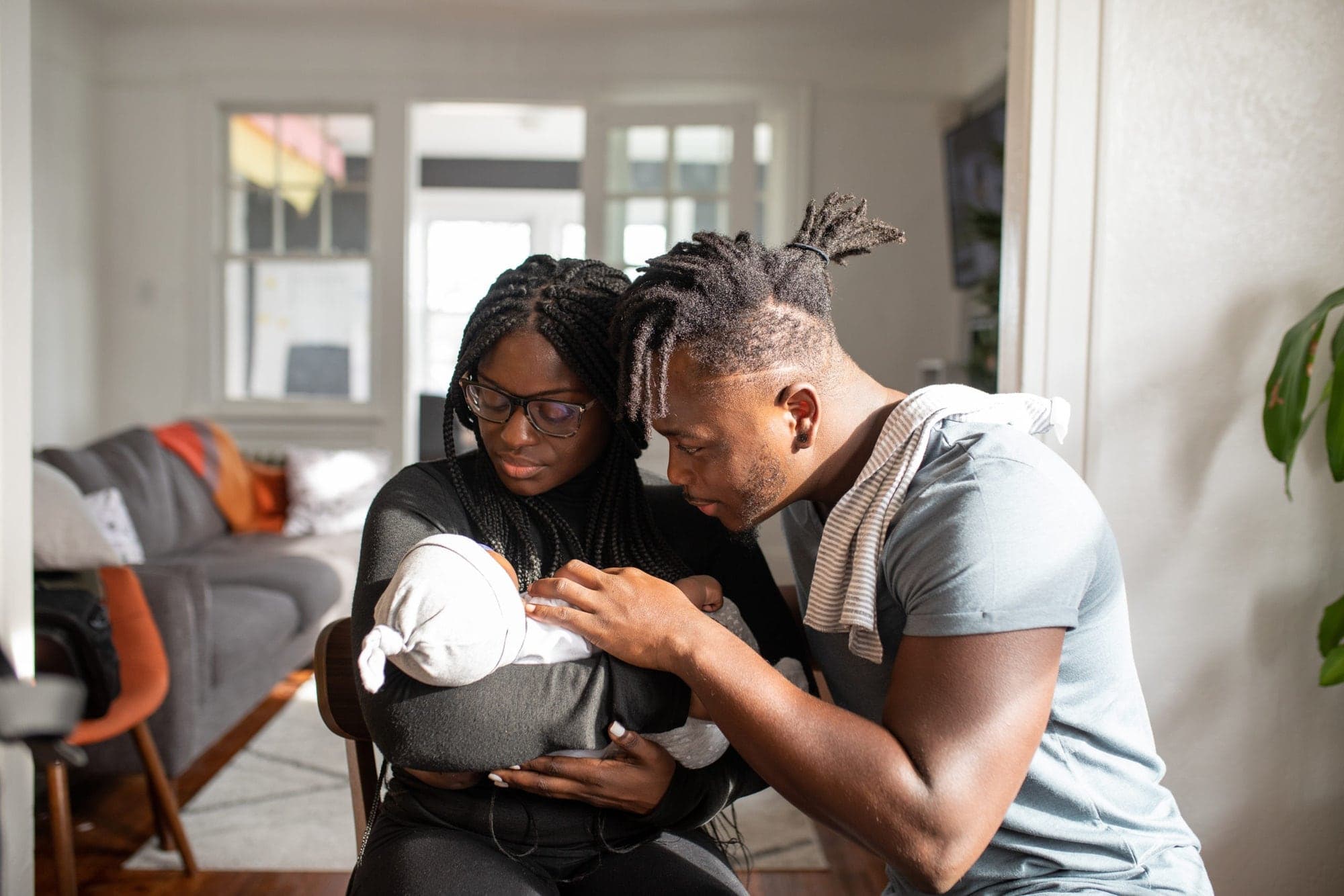 A mother and father leaning in over their newborn on the sofa